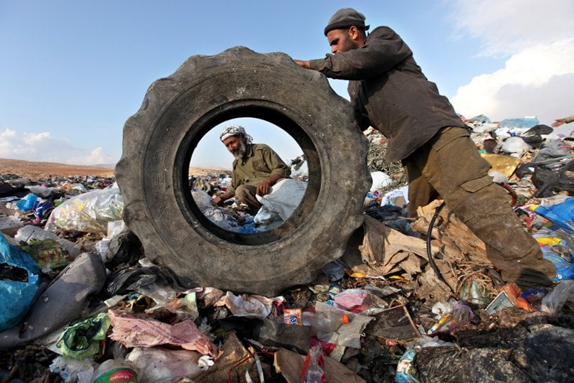 In this October 2011 file photo, Palestinians sift through garbage that was dumped in the West Bank. Some doctors say patients have a right to have causes of illness, especially from environmental pollution, studied as part of their care. Photo: CNS/Abed Al Hashlamoun, EPA 