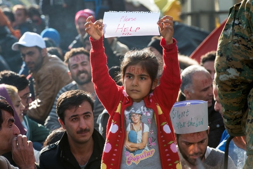 An Iranian girl raises a sheet of paper with 'Please HELP Me' on it Nov. 24 as a group of people wait for permission to cross the border from Greece into Macedonia. PHOTO: CNS