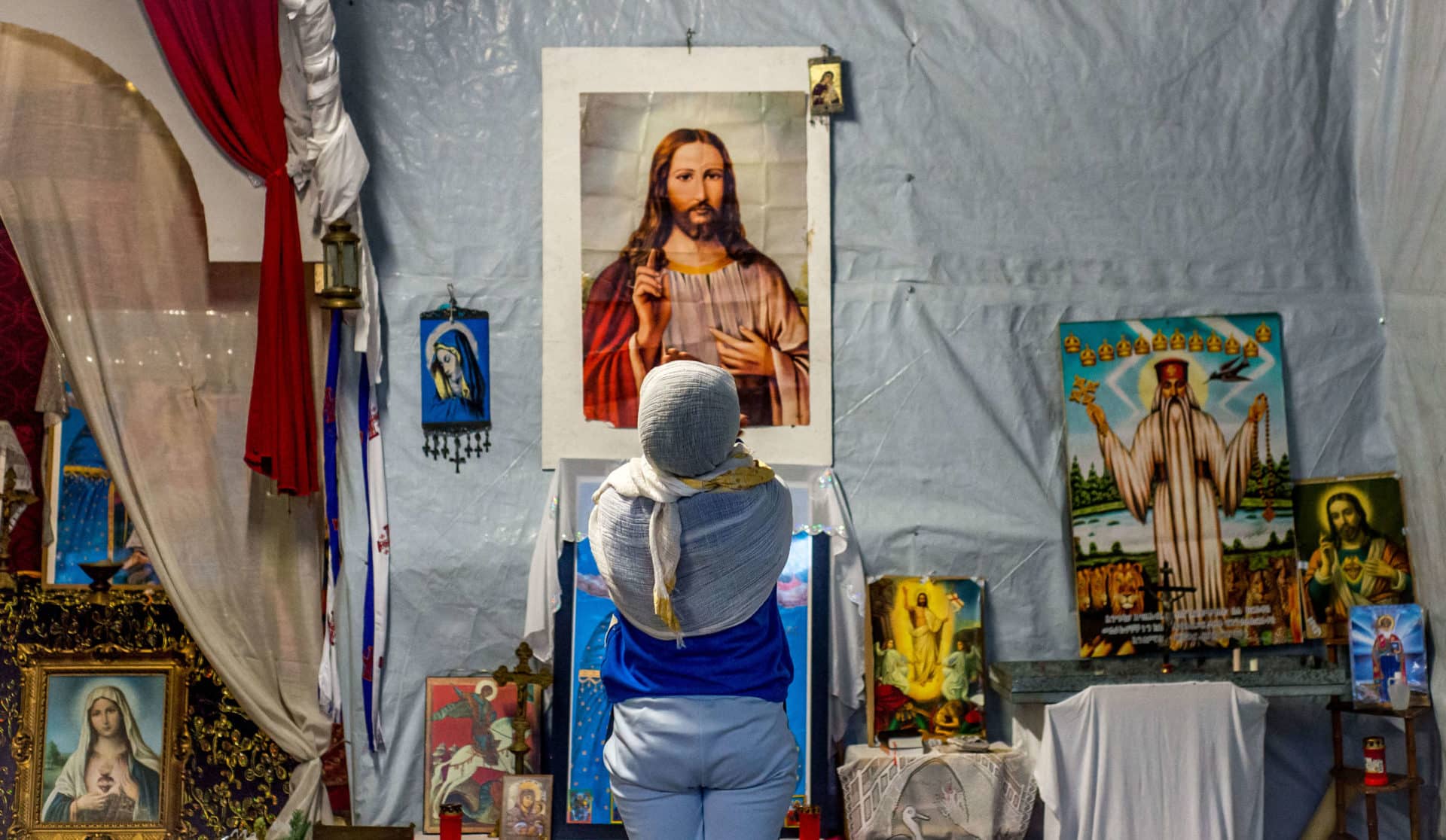 A refugee prays in front of an image of Christ in a makeshift church in a camp called "The Jungle" in 2015 in the port of Calais, France. (CNS photo/Stephanie Lecocq, EPA) See REPORT-FREEDOM May 3, 2016.
