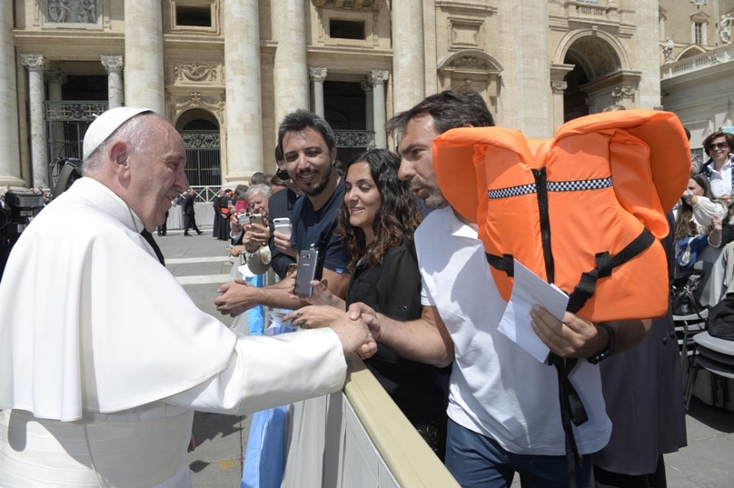 A volunteer from Lesbos, Greece, presents Pope Francis a life-jacket that belonged to a Syrian girl who drowned. The presentation was at the end of the pope's general audience in St. Peter's Square at the Vatican on 25 May. Photo: CNS/L'Osservatore Romano
