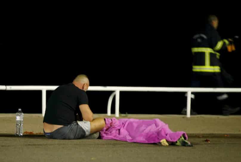 A man sits next to a body on 15 July after at least 84 people were killed in Nice, France, when a truck ran into a crowd celebrating the Bastille Day national holiday on 14 July. Photo: CNS/Eric Gaillard, Reuters