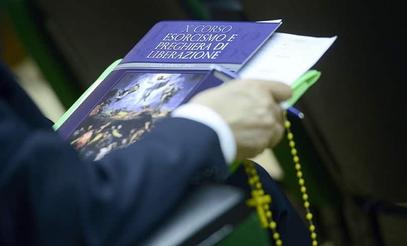 A participant holds a course textbook on exorcism and prayers of liberation.