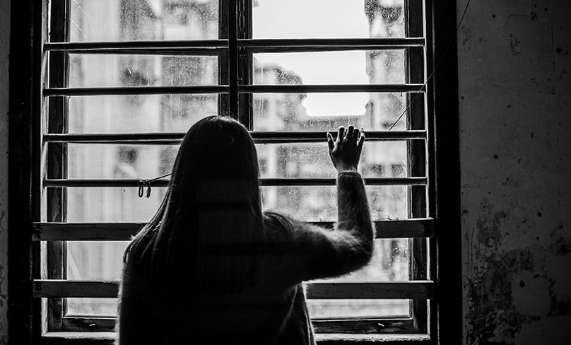 Woman looks through a window from inside a dark room.