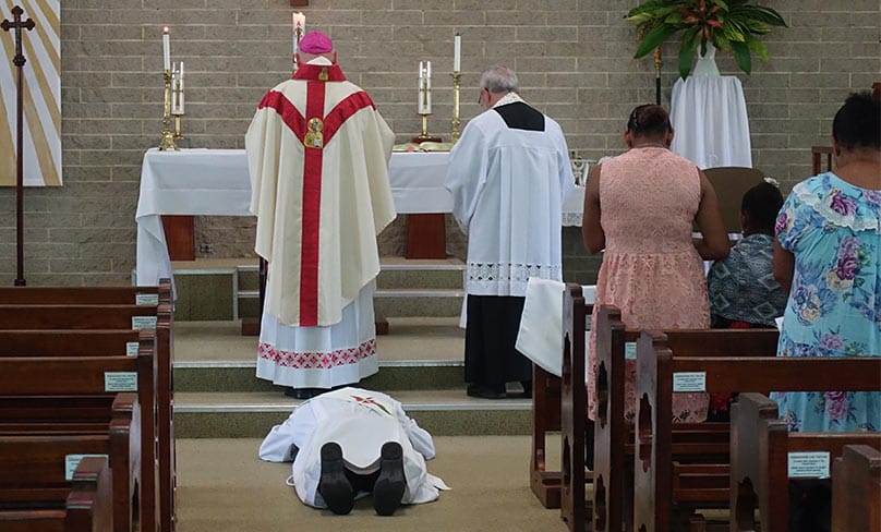 55-year-old Fr Kopel Gibuma prostrates behind Lismore Emeritus Bishop Geoffrey Jarrett In St Francis Xavier Church. Photo: ACBC
