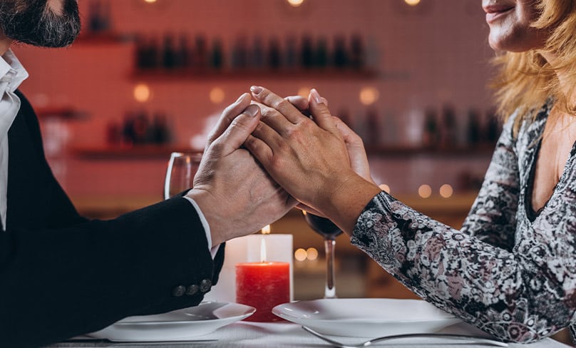 Man and woman holding hands at dinner.