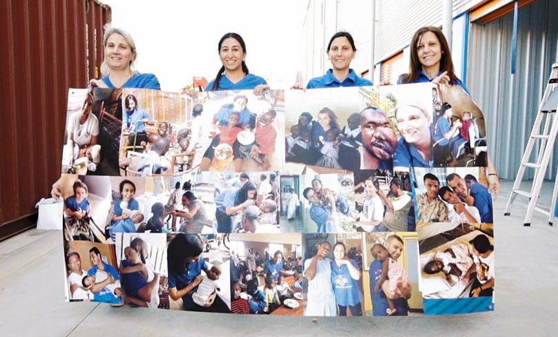 Volunteers with QMHR Hold up a banner with photos from the previous mission to the Missionaries of the Poor Community in Jamaica.