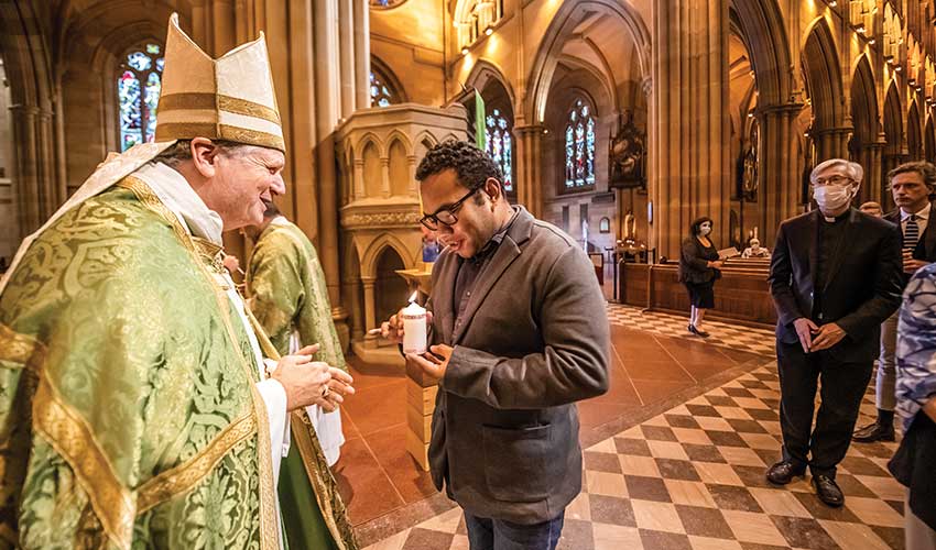 Archbishop Anthony Fisher OP hands a candle to Plenary Council delegate Chris Lee in St Mary’s Cathedral. Photo: Giovanni Portelli