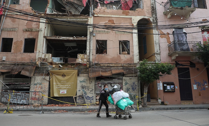 A woman pushes a cart past damaged buildings in Beirut during the COVID-19 pandemic. More than half of the population of Lebanon lives in poverty. Photo: CNS, Mohamed Azakir, Reuters