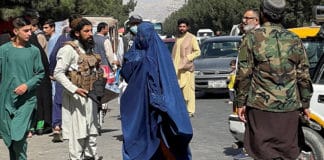 A member of the Taliban forces talks block the roads around Kabul airport as a woman wearing a burqa walks past Aug. 27, 2021. Religious minorities and women are concerned about their treatment at the hands of the Taliban and other religious extremists. Photo: CNS pho
