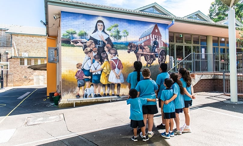 A mindful moment with Saint Mary Mackillop … students of St Jerome’s Punchbowl take time to stop and reflect on the life of Australia’s first saint depicted in a mural by Danny Mulyono. Photo: Giovanni Portelli
