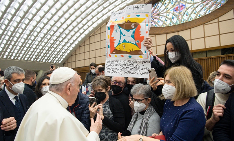 Pope Francis greets people near a banner in Italian calling for the pope’s intervention with Russia, Ukraine and NATO, during his general audience in the Paul VI hall at the Vatican Jan. 19, 2022. Photo: CNS/Vatican Media
