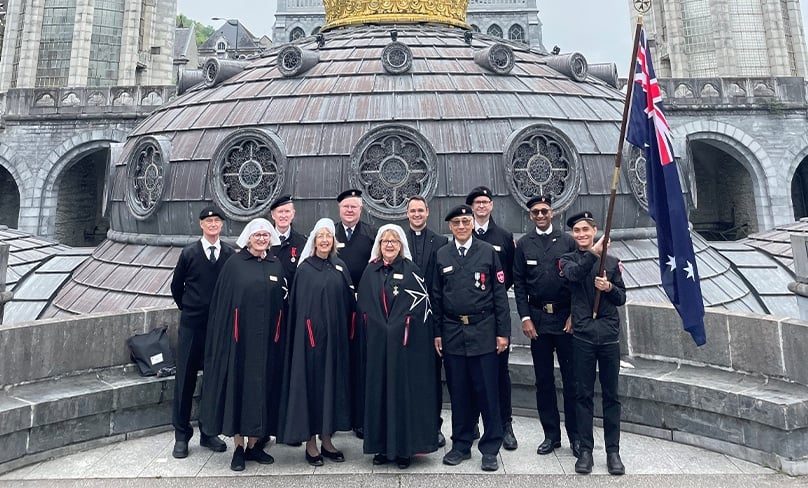 Members of Order of Malta proudly show the flag during their recent pilgrimage to the famed site of Mary’s apparition to St Bernadette Soubirous in 1858. Photo: Courtesy the Order of Malta, Sydney