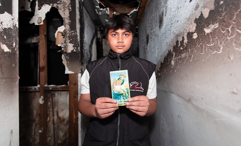 Gabriel, 13, with a treasured prayer card that was left intact in their burnt-out home. Photos: Giovanni Portelli