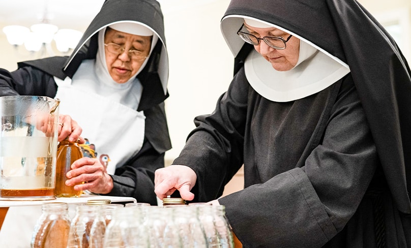 All Saints Sister of the Poor Margaret Muraki, left, and All Saints Sister of the Poor Emily Ann Lindsey screw caps onto jars of honey on the Catonsville, Md., property of the All Saints Sisters of the Poor Aug. 16, 2022. Photo: CNS photo/Kevin J. Parks, Catholic Review