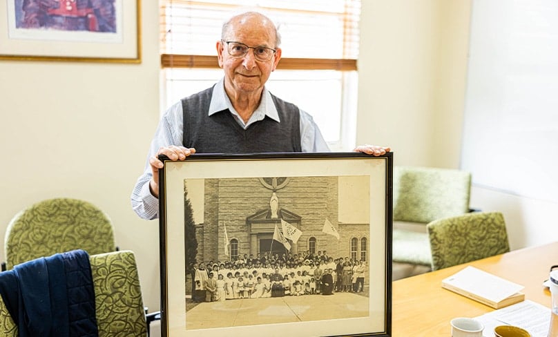 Fr Savino Bernadi cs holds a photo of the annual gathering of the Unanderra Italian Catholic Federation in the early 1970s which still meets today. Photo: Alphonsus Fok