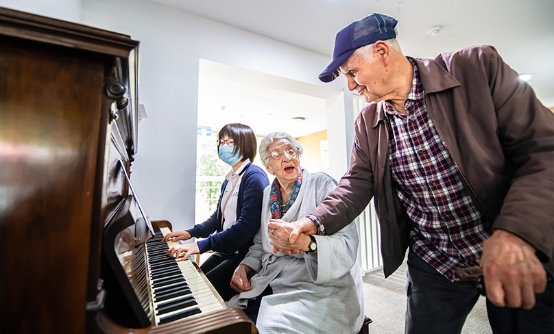 Music’s power: as Katie plays the piano, residents Christine (84) and Dennis Ballas (86) sing along. Katie says the positive effect of music is extraordinary. Often it is the only way of communicating or interacting with some residents where other means have no effect. Photo: Giovanni Portelli