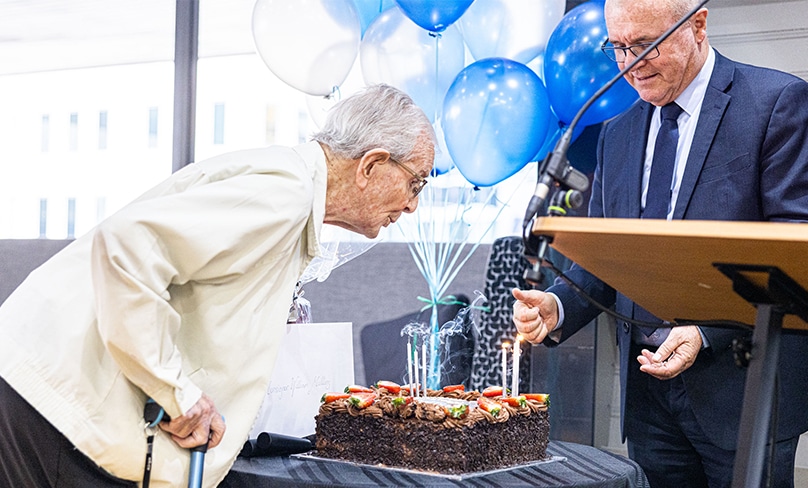 Assisted by Michael Digges, the Archdiocesan Executive Director, Administration and Finance, Monsignor William Mullins blows out the candles at his birthday celebration on 12 April before chatting with staff of the Polding Centre. Photo: Alphonsus Fok