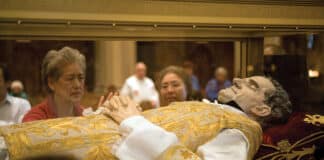 A worshipper looks into a glass casket to view a wax replica of St. John Bosco that contains relics of the saint on display in San Francisco. Photo: CNS/Jose Luis Aguirre, Catholic San Francisco
